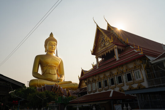 Majestic giant golden Buddha statue and traditional Thai temple hall with sun flare background at Wat Paknam Phasi Charoen in Bangkok, Thailand

