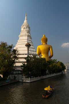 Back view of giant golden Buddha statue and white stupa of Wat Paknam Phasi Charoen temple with longtail boat on canal in Bangkok, Thailand
