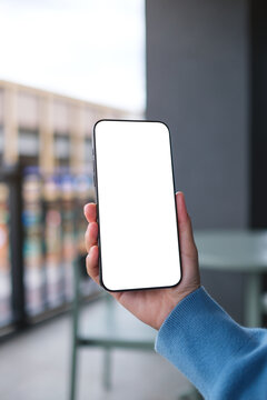 Vertical mockup image of a woman holding and using mobile phone with blank desktop screen in cafe
