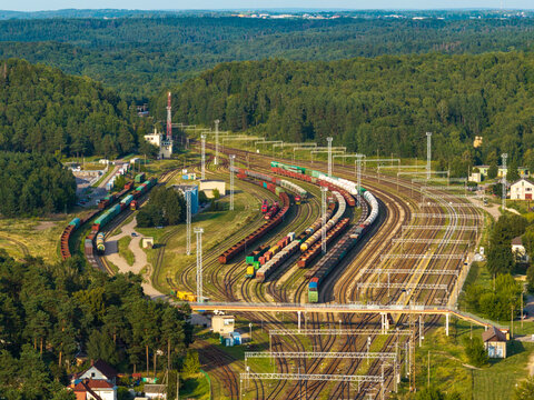 Aerial view of a large railway yard with multiple tracks and freight trains surrounded by dense green forest in Vilnius, Vilnius County, Lithuania.