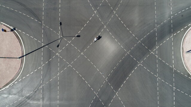 Aerial view of a motorcyclist riding through a large road intersection with white lane markings and a roundabout in Konya, Konya, Turkiye.