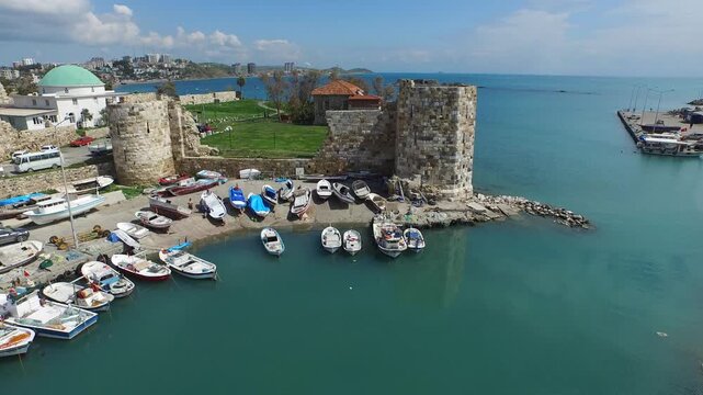 Aerial view of historical castle walls and fishing boats at Mediterranean harbor.