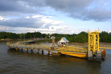 A yellow floating pontoon dock with a crane-like winch structure sits on a calm river beneath a dramatic cloudy sky. © Saipullah