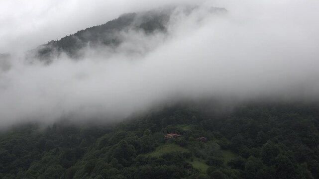 Panoramic fog and forest mountains in Rize Turkey with lone wooden house above valley.