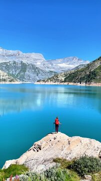 hiker standing on rock overlooking turquoise alpine lake and mountains under blue sky- Freedom, travel, adventure
