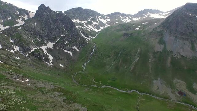 Anzer Rize Turkey valley shows snow patches, green meadows, clear stream, and rugged peaks.