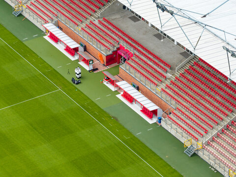 Aerial view of a football stadium sideline with rows of red seats, team benches, and a training field in Poland.