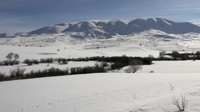 Snowy winter landscape with snow-covered fields and mountains in Xinjiang Uyghur region of China.