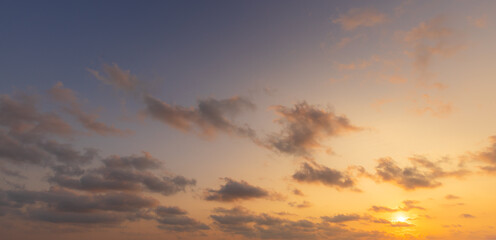 Fototapeta premium Gradient Sky Sunset,A beautiful, serene sunset sky transitions from a deep blue at the top to a warm, glowing golden-yellow near the horizon, filled with scattered, textured clouds. The sun is just.