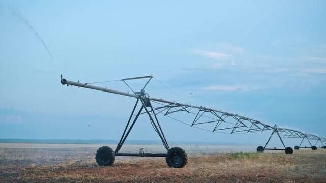 Center pivot irrigation machine on dry farmland at dusk agricultural field landscape, 4K