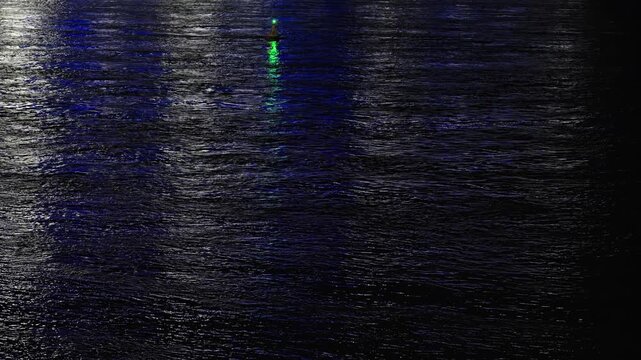 Dark water surface at night reflecting city and buoy lights.