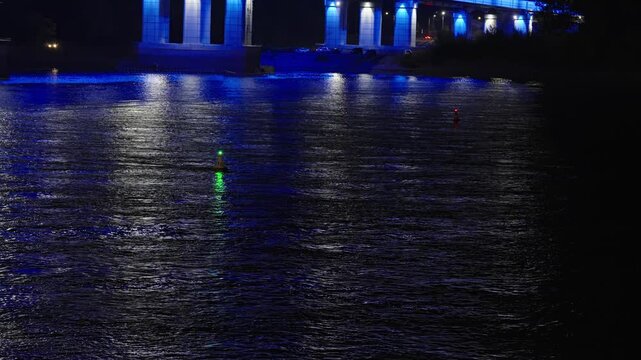 Dark water surface at night reflecting city and buoy lights.