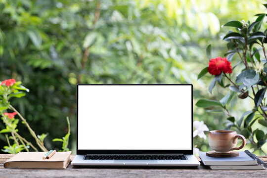 Laptop coffee and earthenware cup and notebooks arranged on table with nature background