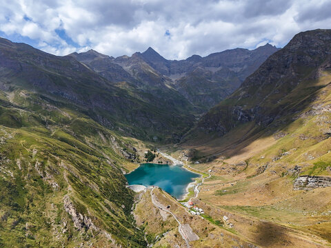 Aerial view of Diga e Lago di Malciaussia, a turquoise alpine lake in a dramatic valley surrounded by rugged mountain peaks and green slopes in Usseglio, Piedmont, Italy.
