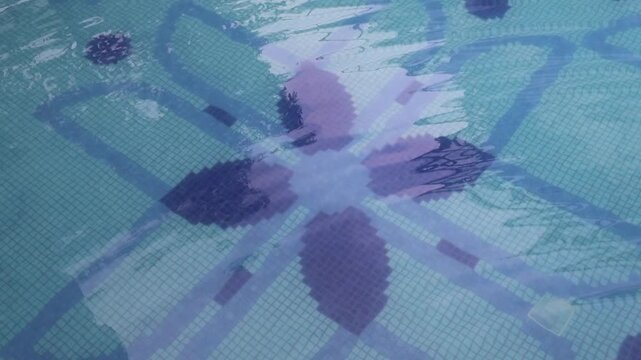 Swimming pool floor with blue mosaic tiles and abstract floral patterns visible beneath clear water. Aquatic texture, underwater geometric pattern, pool background, leisure facility detail