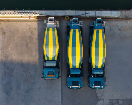 Aerial view of a concrete plant with parked cement mixer trucks on the quay and a boat navigating the canal in Akersloot, Noord-Holland, Netherlands.