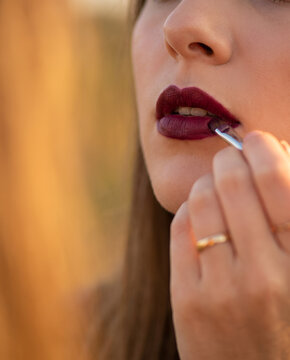 Woman applying burgundy lipstick with brush in detailed close-up macro