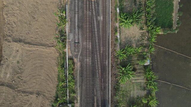 Aerial Top-Down View of a Train Passing Through Farmlands on One Track of a Double-Track Railway. Passenger Railway Creates a Strong Geometric Pattern Across the Rural Landscape in Indonesia.