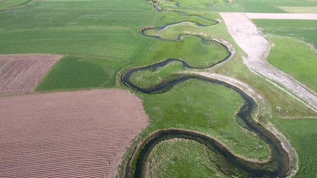 Meandering river winds through patchwork farmland, shaping green and brown floodplain fields.
