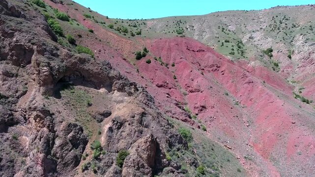Exposed mineral outcrop reveals red strata and ore bearing layers across a barren slope.