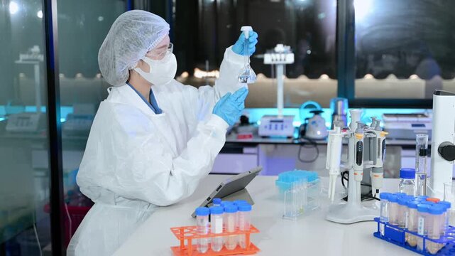 Focused researcher in protective lab gear examines scientific specimens using a stereo microscope in a modern biotechnology laboratory.