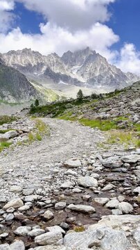 Scenic trail leads through alpine rocky valley toward majestic mountain peaks under blue sky- French alps