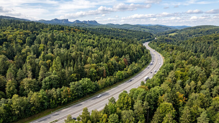 Fototapeta premium Aerial View of a Winding Highway Cutting Through a Vast Evergreen Pine Forest at Sunset