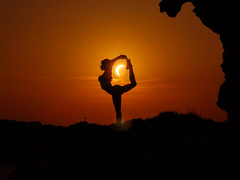 Ciutadella, Balearic Islands, Spain - 12 August 2026: Aerial view of a silhouette of a person performing a yoga pose against the backdrop of a solar eclipse.