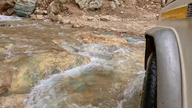 Low Angle POV Of 4x4 Vehicle Crossing Fast Flowing Rocky Mountain Stream