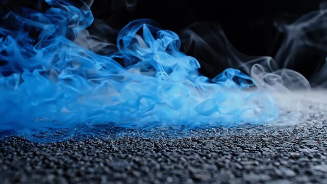 Extreme close-up of thick blue smoke and misty fog swirling over dark asphalt pavement with a black defocused background