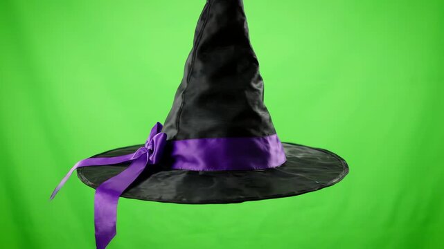 Floating black witch hat with purple ribbon spinning slowly in a seamless loop against a bright chroma key green screen background