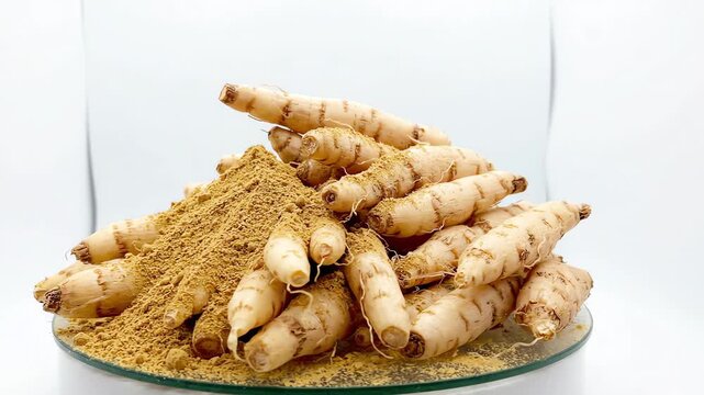 Rotating pile of fresh shatavari roots with fine ground herbal powder on a plain white studio background