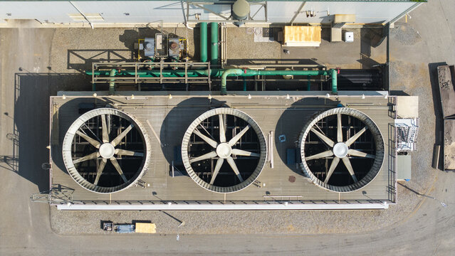 Aerial view of an industrial cooling tower unit featuring three large fans on a flat roof with green piping and surrounding paved ground in Plainfield, Connecticut, United States.