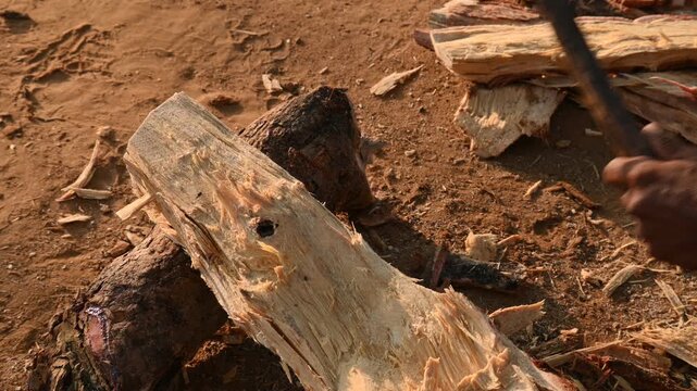 A person using a traditional hand axe to hew a rough wooden log resting. Traditional manual wood-chopping axe with a metal head and wooden handle. Its Commonly used in rural and village settings.