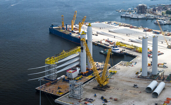 Aerial view of wind turbine construction site at the port with large cranes, turbine blades, and tower sections being prepared for assembly in New London, Connecticut, United States.