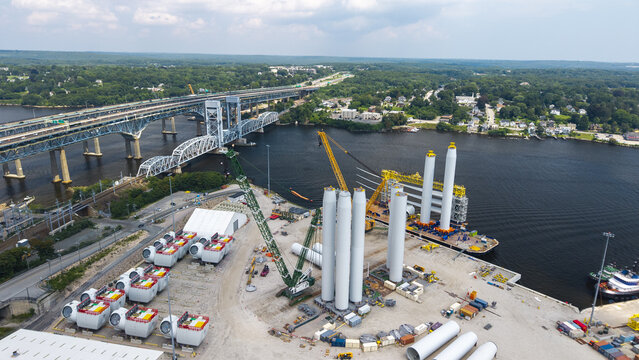 Aerial view of wind turbine construction site at the port with turbine towers, nacelles, and cranes positioned near the river and bridge in New London, Connecticut, United States.