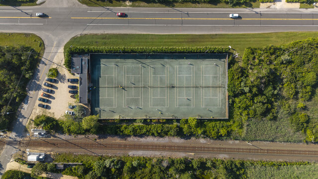 Aerial view of the tennis courts on Long Island surrounded by lush greenery, adjacent to a road with parked cars and railway tracks in New York, United States.