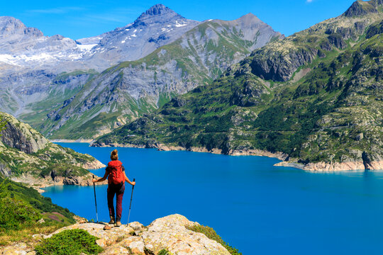 Female hiker with red backpack looking at blue alpine mountain lake view