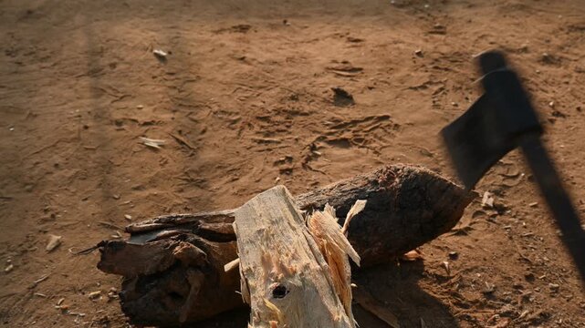 A person using a traditional hand axe to hew a rough wooden log resting. Traditional manual wood-chopping axe with a metal head and wooden handle. Its Commonly used in rural and village settings.