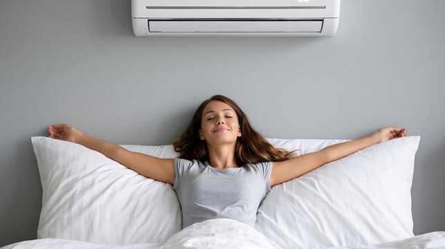 Woman enjoys cool air from a climate control unit while resting in bed.