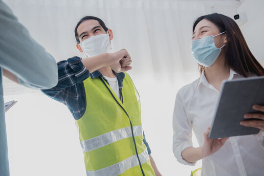Engineers greeting with elbow bump while wearing face mask during construction meeting