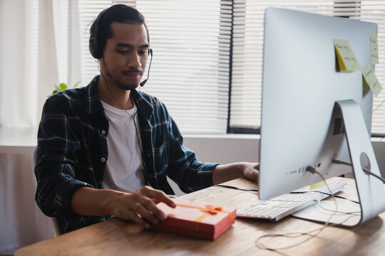 Man with headphones holding gift box during online video call at home office