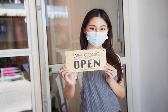 Small business owner wearing mask holding open sign at shop entrance