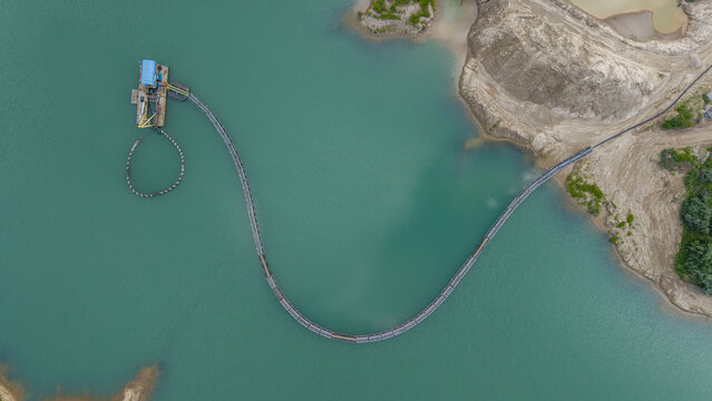 Aerial view of a gravel factory dredging operation with a floating dredge and a long pipeline extending across the turquoise lake water in Middle Island, New York, United States.