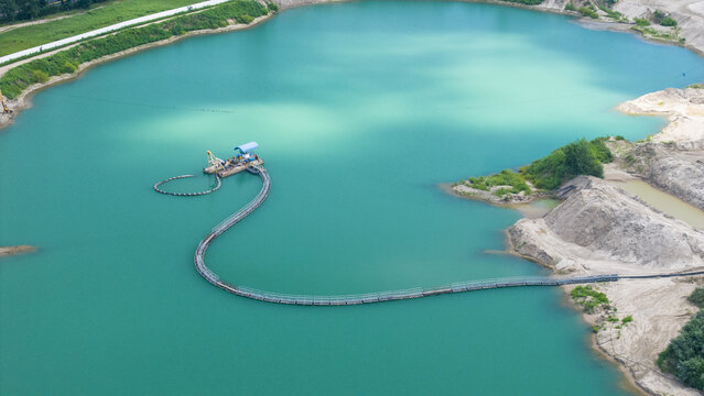 Aerial view of a gravel factory dredging operation in a turquoise quarry pond with sandy banks and a floating pipeline in Middle Island, New York, United States.