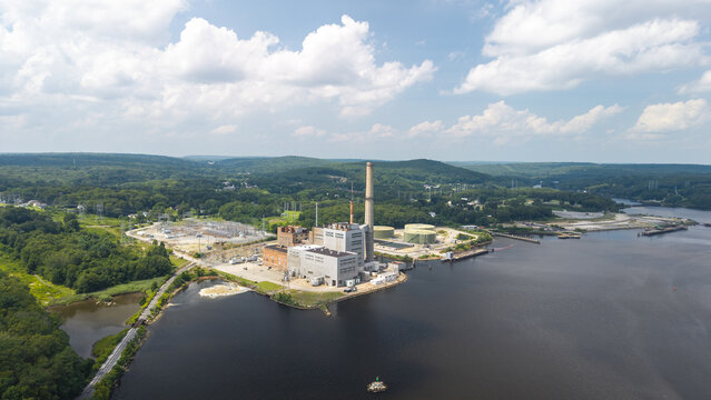 Aerial view of Generation Bridge Montville Power plant on the Thames River, surrounded by dense forests and rolling hills under a blue sky in Montville, Connecticut, United States.