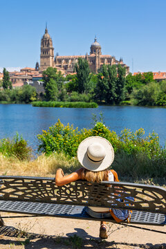Woman sitting on park bench admiring view of Salamanca Cathedral over Tormes river in Spain