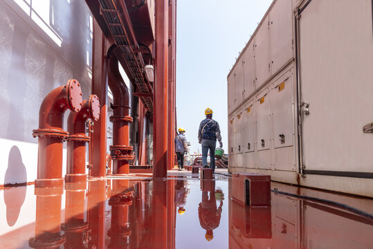 Workers walking aboard a newly constructed vessel, viewed from behind as they move toward different work areas during shipbuilding operations.