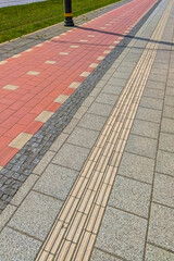 Obraz premium Modern urban sidewalk with a red bicycle lane and tactile paving for visually impaired people. Accessible city infrastructure and inclusive urbanism concept.
