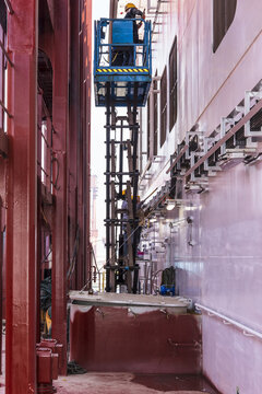 Shipyard worker carrying out manual cleaning and painting work in an industrial shipbuilding environment during vessel completion.